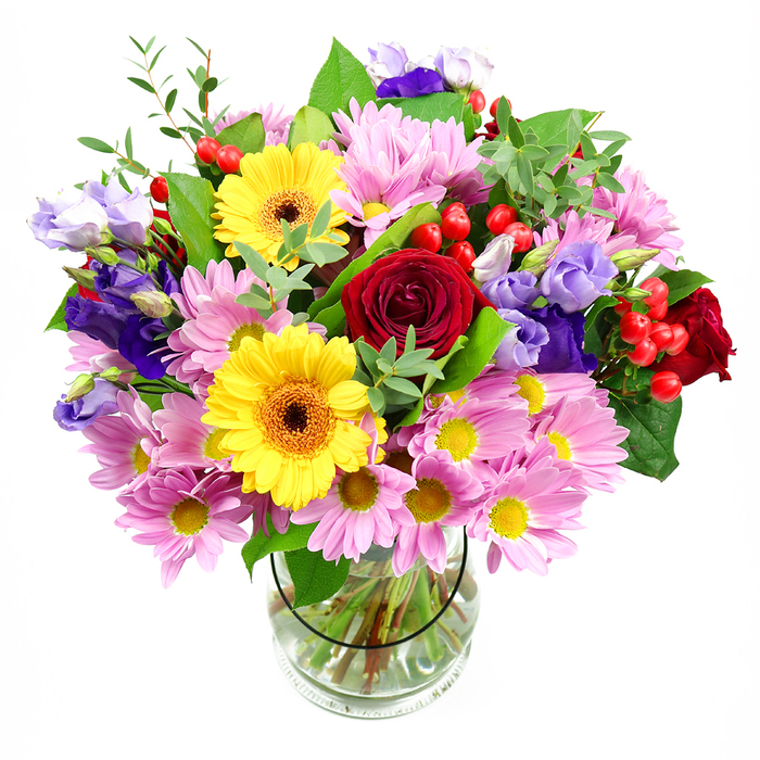 This photograph shows a lush, exuberant bouquet arranged with the care and balance of an experienced Shooter's Hill florist, displayed in a simple clear glass vase against a bright white background. The central focus is a cluster of deep red roses, each bloom opening in soft spirals, their rich, velvety petals suggesting romance and warmth. Nestled among them are two vibrant yellow gerbera daisies, their cheerful faces edged with layered petals and anchored by dark brown-orange centres, adding a sunny, upbeat character that feels perfect for a celebration or thank-you delivered to a home off Shooters Hill Road. Encircling these main blooms is an abundant ring of pink daisy chrysanthemums, each flower formed by many slender petals around small yellow hearts, lending the arrangement a feathery softness and a sense of generous fullness. Threaded through the pinks and reds are cool purple and lavender lisianthus, their bell-like shapes and softly ruffled edges introducing subtle movement, as though they are gently leaning toward the light. Bright red hypericum berries dot the bouquet like tiny ornaments, their smooth, rounded forms providing an appealing contrast to the petal textures. Various shades of green foliage weave throughout, with broad, dark leaves adding depth and lighter, airy sprigs lifting the composition, echoing the layered greenery you might see walking towards Oxleas Wood. The stems are clearly visible through the transparent vase, neatly trimmed and fanned in clear water, which grounds the otherwise expansive, airy top. Even, neutral lighting enhances the true colours without harsh shadows, giving the overall impression of a fresh, joyful mixed-flower arrangement ready to become a dining table centrepiece or a heartfelt gift for any milestone in Shooter's Hill.