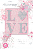 This anniversary card offers a tender portrait of enduring romance, rendered in soft pastel pinks, silvery greys, and pearly whites that feel as serene as a late afternoon sky seen from the paths around Shooter's Hill. At the centre of the design, the word LOVE stands in raised, softly glittering letters, each stroke edged in fine sparkle that shivers in the light. The O is transformed into a shimmering silver heart, textured so it appears almost like a tiny metal charm set gently into the card. This tactile heart becomes the quiet focal point, a symbol of constancy and shared time. Around it, delicate blossoms in blush, mauve, and barely-there ivory unfurl in an almost watercolour softness, their outlines fluid and graceful. They weave with slender vines and flourishes, evoking the gentle structure of an English spring garden or a thoughtfully composed bouquet prepared for delivery across the local SE18 area. Tiny petals, looping swirls, and discreet butterflies introduce a sense of motion, as though a soft breeze were drifting across the design. The text On Our Anniversary and I love you today and always is written in an understated script, its flowing lines mirroring the curves of the vines and stems. The whole composition feels calm and intimate, the kind of card you might tuck beside a vase of fresh anniversary flowers in a Shooter's Hill home-a quiet but deeply meaningful keepsake that honours years of shared memories, whispered promises, and gentle companionship.